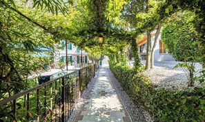 A pathway lined with greenery and a metal fence, leading to a building with a white facade and green shutters. - EXPERIENCE THE ELEGANCE OF THE FRENCH RIVIERA IN THIS EXCEPTIONAL 300 M² VILLA (Cannes)