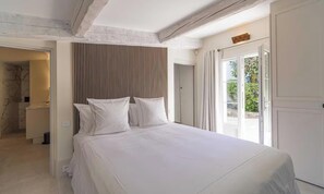A bedroom with a large bed, a wooden headboard, and a view of the outdoors through a door. - EXPERIENCE THE ELEGANCE OF THE FRENCH RIVIERA IN THIS EXCEPTIONAL 300 M² VILLA (Cannes)