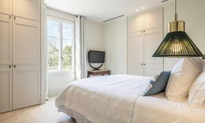 Un dormitorio con cama, televisor en una mesita de noche y ventana con cortinas.
