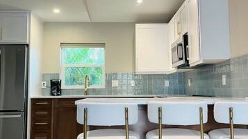 A modern kitchen with a central island, bar stools, and a refrigerator.