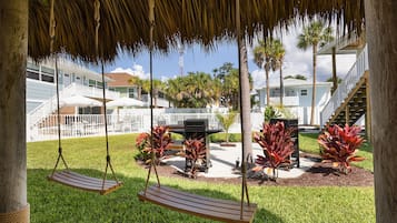 A covered outdoor area with a swing set, a grill, and a pool.