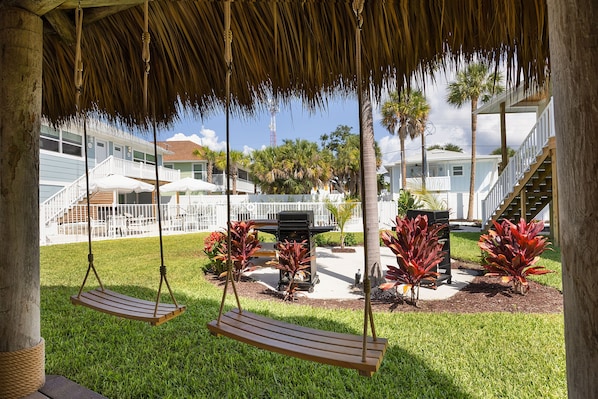 A covered outdoor area with a swing set, a grill, and a pool. - The Woods (Fort Myers Beach)