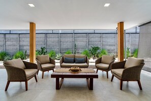 Een terrasgedeelte met rieten meubels, een centrale salontafel en uitzicht op een tuin met diverse planten.