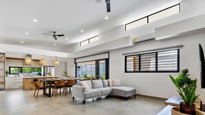 A spacious living area with a grey sectional sofa, a dining table with chairs, and a kitchen in the background. - Villa con Piscina Privada a 3 min de la Playa / Concierge incluido (Playa Grande)