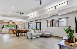 A spacious living area with a grey sectional sofa, a dining table with chairs, and a kitchen in the background. - Villa con Piscina Privada a 3 min de la Playa / Concierge incluido (Playa Grande)