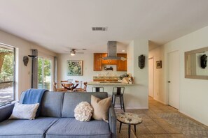 A modern living room with a grey sofa, a small round table, and a dining area with a wooden table and chairs. - 5 bed/5 bath Hiking on Greenbelt Close to Zilker! (Austin)