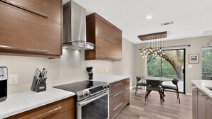 Una cuina moderna amb armaris de fusta, una campana extractora d'acer inoxidable i una zona de dinar amb vista a arbres.