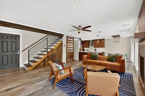 Ein modernes Wohnzimmer mit einer Couch, Sesseln, einem Couchtisch und einer Treppe.