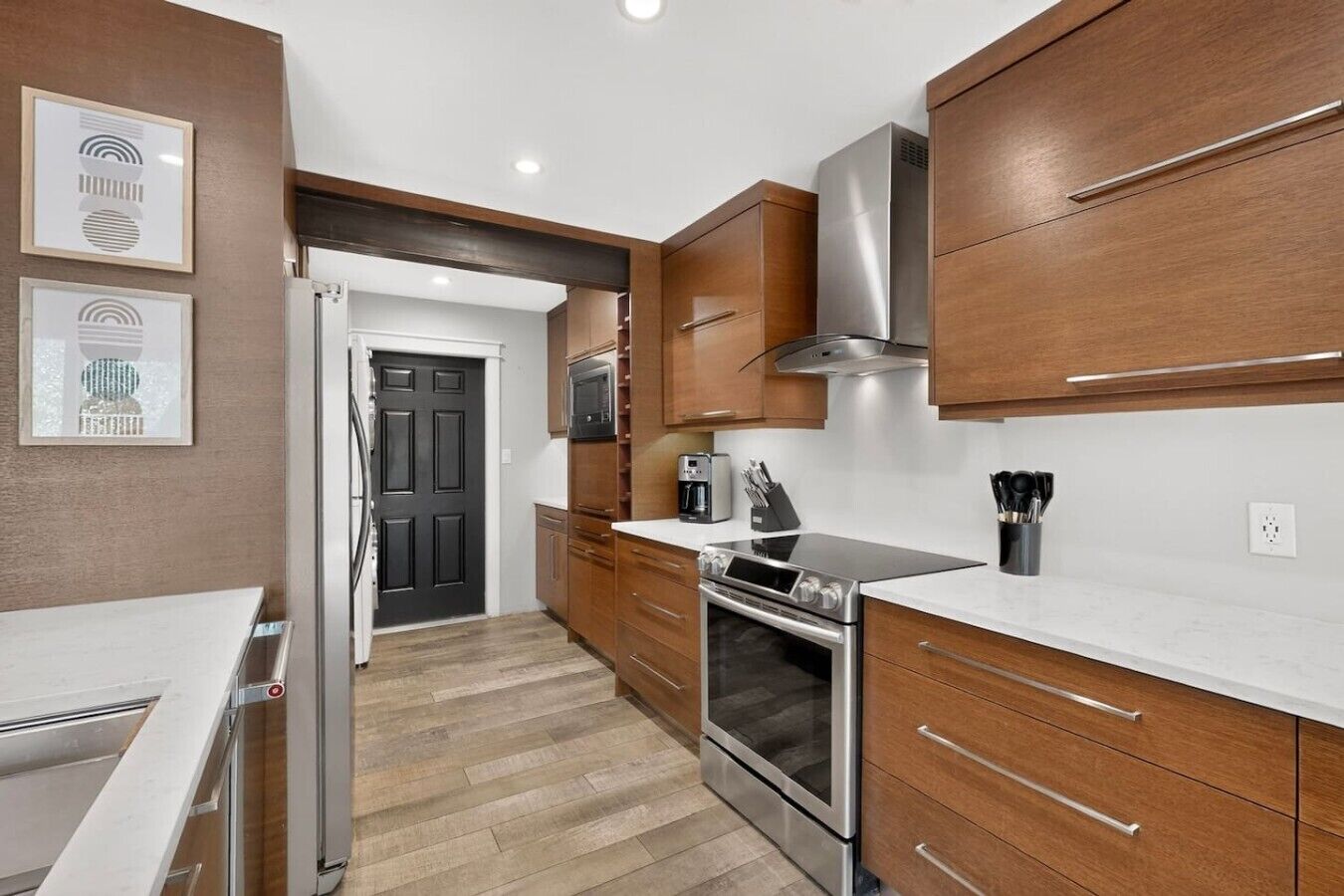 A modern kitchen with wooden cabinets, a stainless steel range hood, a built-in oven, and a countertop with a coffee maker.