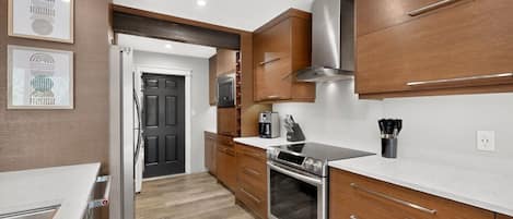 A modern kitchen with wooden cabinets, a stainless steel range hood, a built-in oven, and a countertop with a coffee maker.