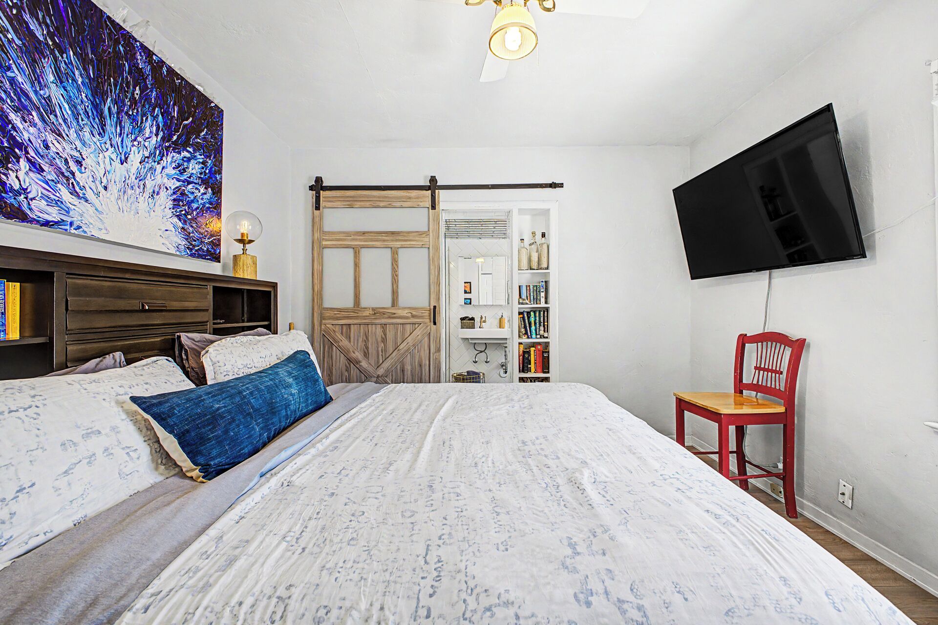 A bedroom with a bed, a television mounted on the wall, and a bookshelf.