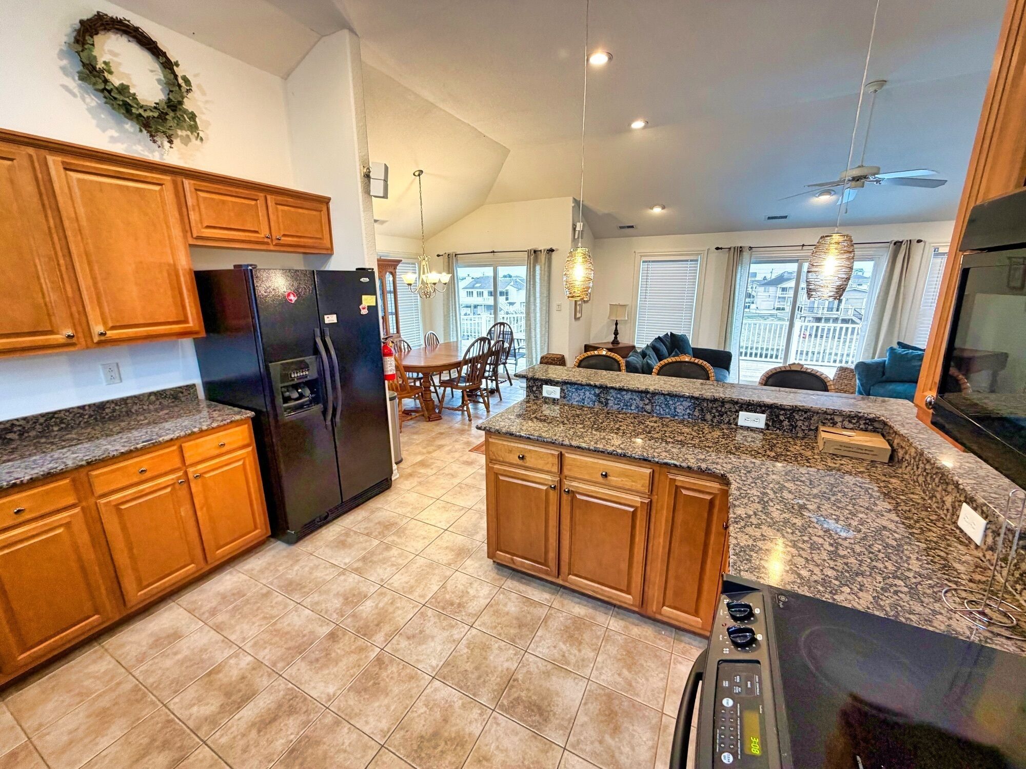 A kitchen with granite countertops, wooden cabinets, a black refrigerator, and a dining area with a table and chairs.