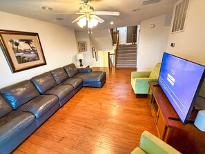 A living room with a sectional sofa, a television, and a staircase leading to an upper level. - Serenity Sound House Sandbridge Oasis With Pool (Virginia Beach)