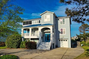 A two-story house with a blue roof, a front porch with a blue door, and a garage. - Serenity Sound House Sandbridge Oasis With Pool (Virginia Beach)