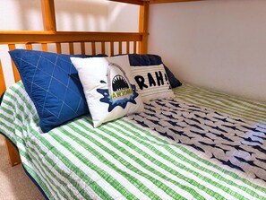 Un letto con lenzuola a righe e due cuscini, uno con un disegno di squalo e la scritta 'RAWR!'