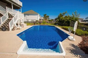 A swimming pool with a clear blue water surface, surrounded by a concrete deck, a white fence, and a staircase leading to a building. - Serenity Sound House Sandbridge Oasis With Pool (Virginia Beach)