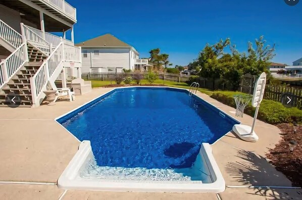 A swimming pool with a clear blue water surface, surrounded by a concrete deck, a white fence, and a staircase leading to a building. - Serenity Sound House Sandbridge Oasis With Pool (Virginia Beach)