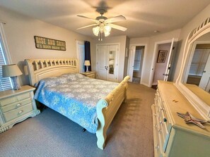 A bedroom with a bed, dresser, mirror, ceiling fan, and a wall sign. - Serenity Sound House Sandbridge Oasis With Pool (Virginia Beach)