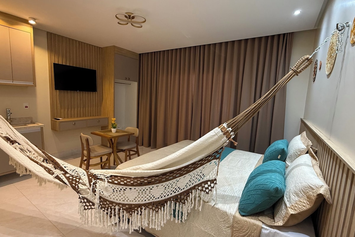 Een moderne hotelkamer met een hangmat, een bed met behang, een kleine tafel met stoelen, een televisie en een keukenhoek.