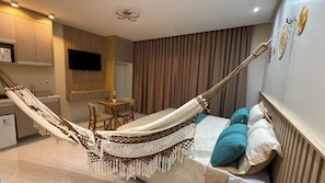 Een moderne hotelkamer met een hangmat, een bed met behang, een kleine tafel met stoelen, een televisie en een keukenhoek.