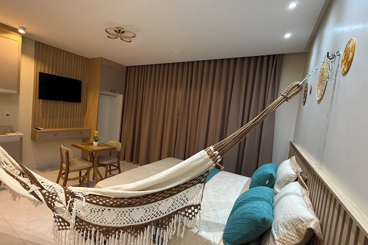 Een moderne kamer met een hangmat, een bed met kussens, een klein tafeltje en een aan de muur bevestigde televisie.