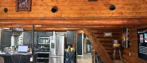 A rustic cabin interior with a kitchen, dining area, and a dog.