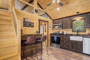 A wooden cabin interior with a kitchen, two bar stools, a microwave, and a wooden staircase. - Brand New!  2-bedroom cabin with AC in scenic Sevierville. (Sevierville)