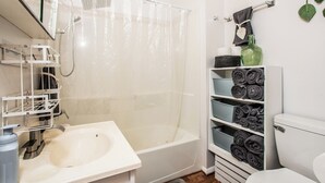 A bathroom with a bathtub, a toilet, and a shelf with towels.