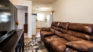 A living room with a brown leather sofa, a flat-screen TV, and a decorative vase.
