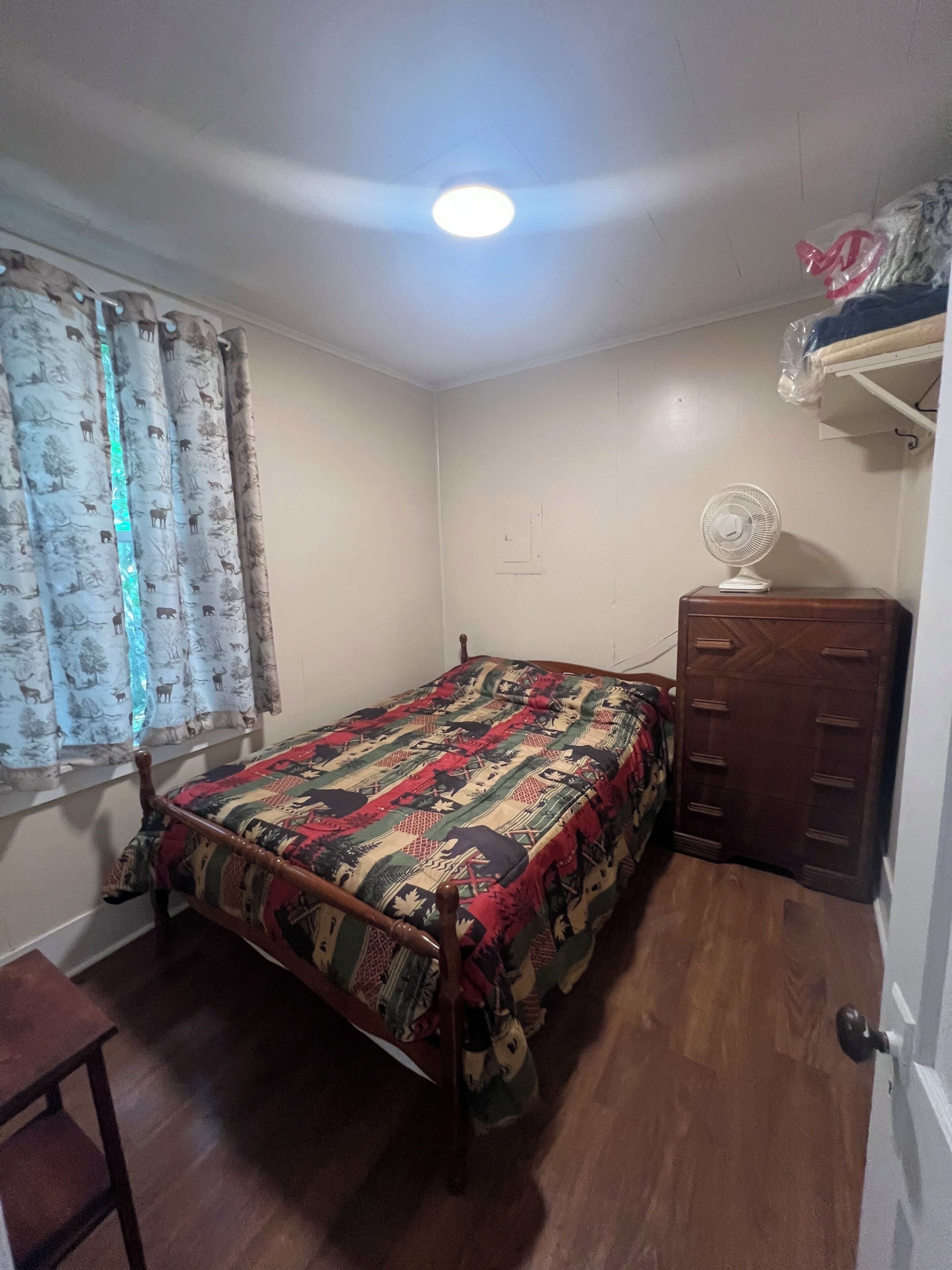 Una camera da letto con un letto, una cassettiera in legno, una ventola a soffitto e una finestra con tende.