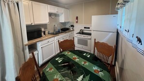 Cocina compacta con armarios blancos, microondas, estufa y refrigerador.