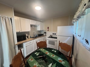 A compact kitchen with white cabinets, a microwave, a stove, and a refrigerator.