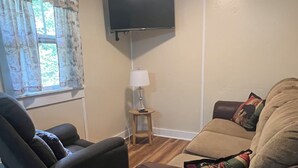 Una sala de estar con sofá, sillón y televisor montado en la pared.