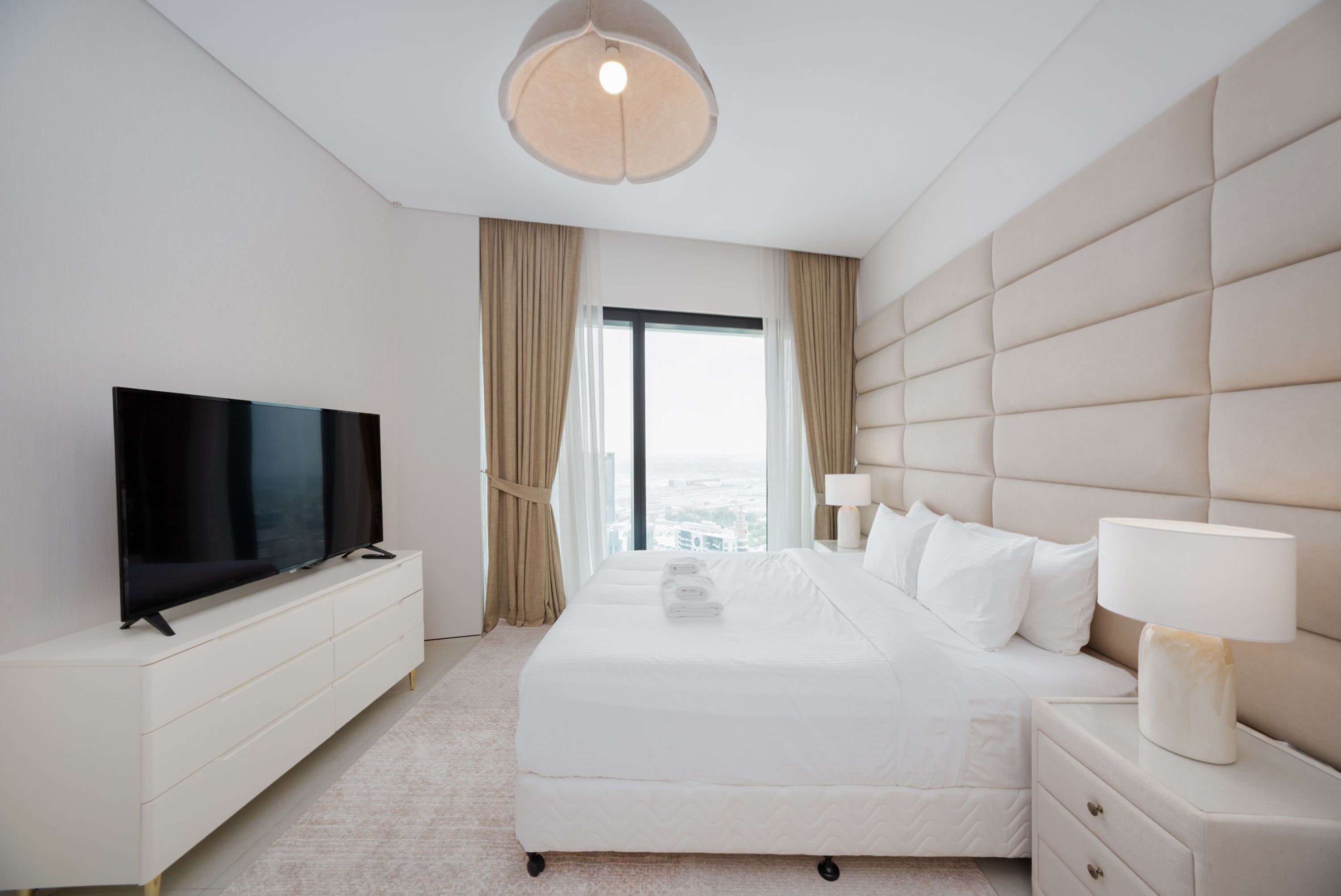 Une chambre d’hôtel avec un grand lit, un téléviseur à écran plat, une table de chevet avec une lampe et une vue sur la ville par la fenêtre.