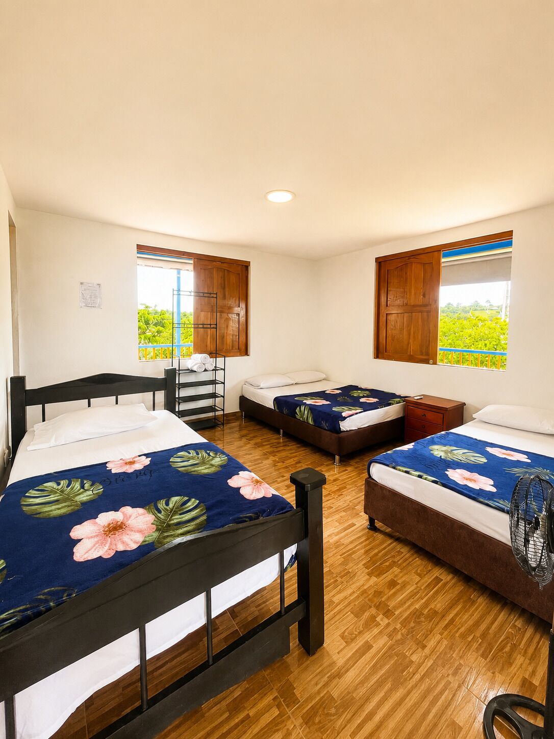 A room with three beds, wooden flooring, and windows with wooden shutters.