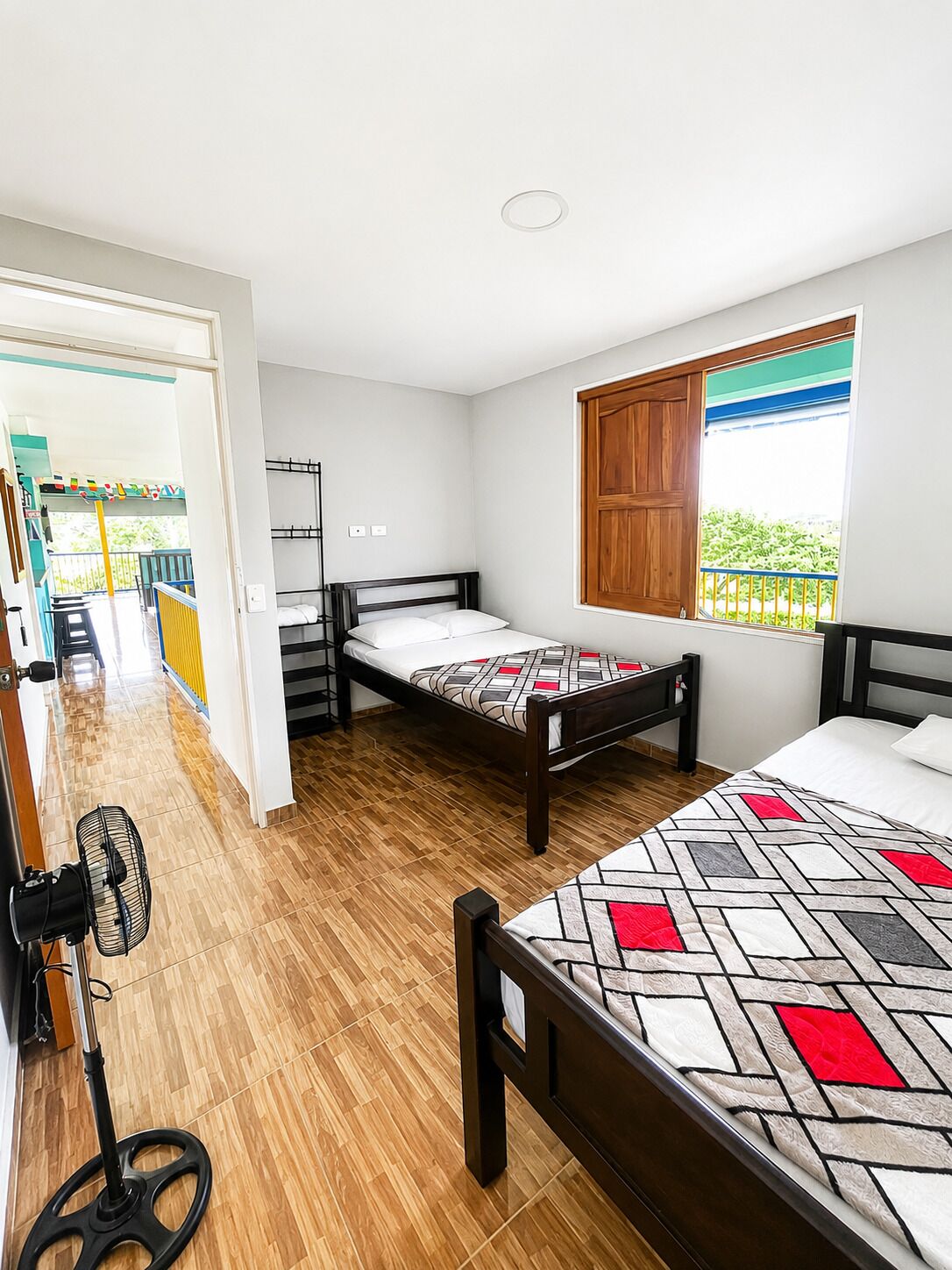 Ein Zimmer mit zwei Betten, einem Fenster mit Blick, einem Ventilator und einer Tür, die auf einen Balkon führt.