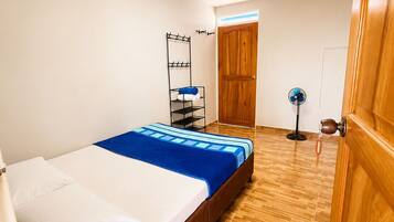 A bedroom with a bed, wooden flooring, a wardrobe, a fan, and a wall-mounted shelf.