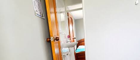 A room with a bed, a wooden door, a white wall, and a bathroom visible through the door.