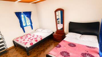 A bedroom with two beds, a wooden ceiling, a window with blue curtains, and a mirror.
