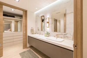 Une salle de bain moderne avec un meuble-lavabo à deux vasques, un grand miroir et une porte en bois donnant sur une chambre.