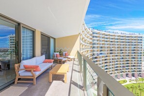 Ein Balkon mit einer Couch und Stühlen, einem Holztisch und Blick auf ein Hochhaus.