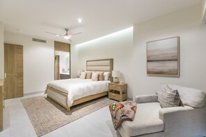 Une chambre moderne avec un grand lit, des tables de chevet, une commode, un canapé, un ventilateur de plafond et un tableau au mur.