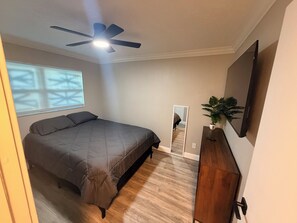 A bedroom with a bed, a ceiling fan, a potted plant, a mirror, and a TV on the wall. - Cozy 2-bedroom, 2 bathroom house just minutes from Sanibel and Fort Myers Beach! (Fort Myers)