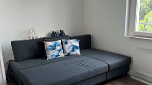 A modern living room with a grey sofa, white armchairs, and a window with a view of greenery.