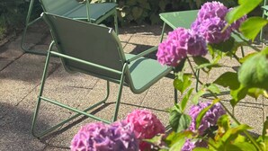 A patio area with metal chairs and a small table, surrounded by a brick wall and greenery.
