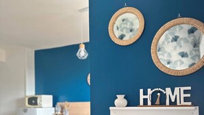 A kitchen with a blue wall, two wall-mounted mirrors, a shelf with a decorative item, and a refrigerator.