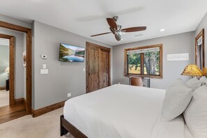 Ein Schlafzimmer mit Bett, Deckenventilator, Fernseher, Fenster mit Blick und einer Tür.