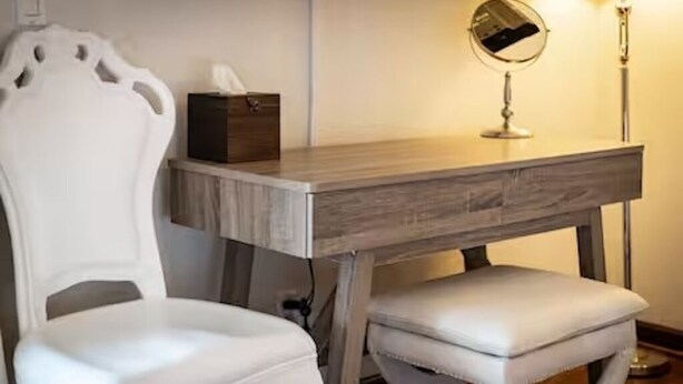 Una silla blanca con tapicería y un reposapiés junto a una cómoda de madera con un espejo y una caja.