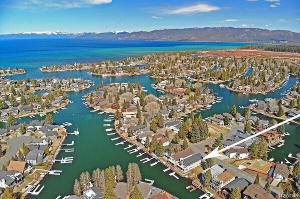 Un quartier résidentiel avec des maisons et des bateaux amarrés le long d’un canal sinueux, entouré d’arbres et avec des montagnes en arrière-plan.