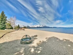 Ein Strand mit blauem Himmel, sandigem Ufer und einem Bergzug im Hintergrund.